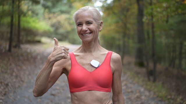 Mature woman smiles and gives a thumbs up while monitoring her heart activity outdoors, promoting health and wellness