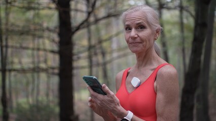 Mature woman checks her heart monitor during a peaceful moment in the woods, promoting health and wellness awareness