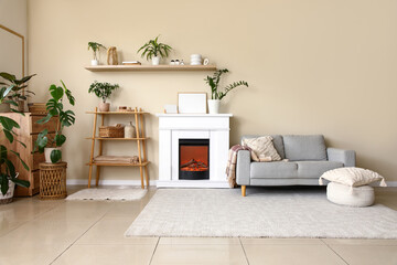 Naklejka premium Interior of living room with fireplace, shelving unit and grey sofa near beige wall
