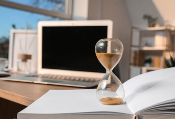 Fototapeta premium Hourglass on book in office, closeup