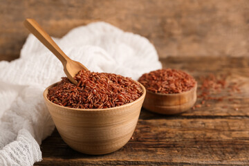 Bowl and spoon with raw brown rice on wooden background