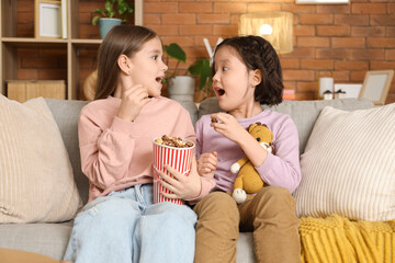 Shocked girls with popcorn watching cartoons on sofa at home