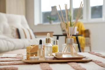 Reed diffuser with burning candles and essential oils on table in living room, closeup