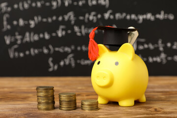 Piggy bank with graduation hat and coins on table near blackboard. Student loan concept