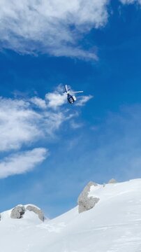 LOW ANGLE VIEW: Helicopter takes off a snowy mountain and flies towards valley. Flight transport for adventurous freeride heliskiing in picturesque and untouched wild mountains of spectacular Albania.
