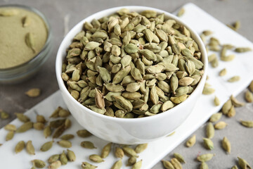 Bowls with cardamom spice and powder on grey background, closeup