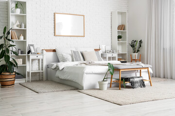Big comfortable bed near white brick wall in interior of bedroom