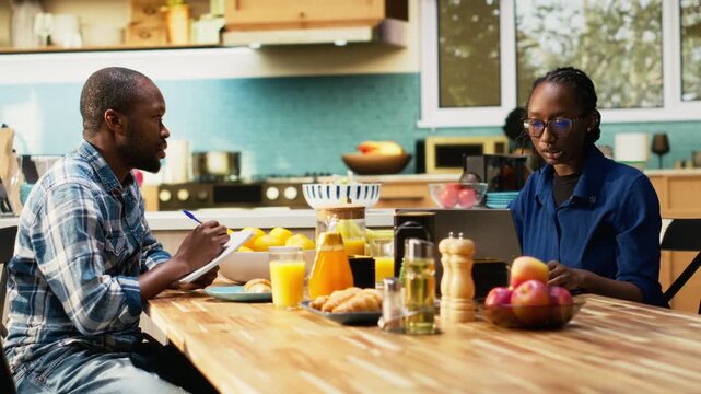 African American couple writing a grocery list together on a laptop. Man and woman planning shopping for essentials, groceries and household products online, healthy eating habits. Camera B.