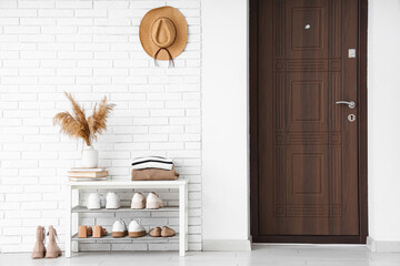 Stand with stylish shoes near white brick wall in interior of modern hallway