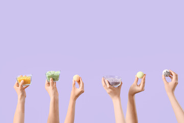 Female hands holding bowls with sea salt and bath bombs on lilac background
