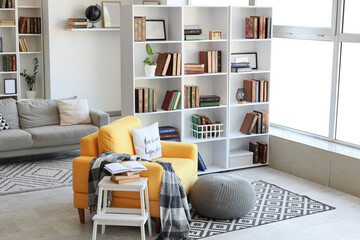 Fototapeta premium Interior of stylish living room with yellow armchair, pouf and bookshelf
