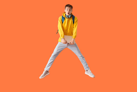 Shocked male student with laptop jumping on orange background