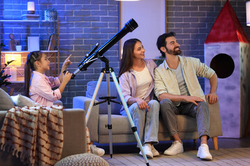 Little girl with her parents and telescope at home in evening