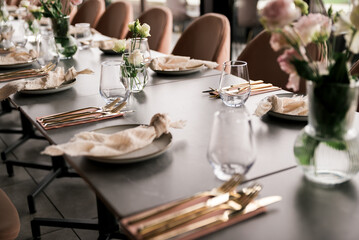 Close-up of an elegant event table setting with gold cutlery, neutral linens, glassware, and soft floral arrangements, creating a refined and modern atmosphere for celebrations or fine dining.