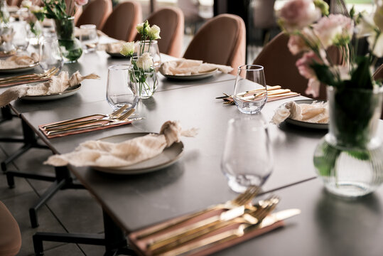 Close-up of an elegant event table setting with gold cutlery, neutral linens, glassware, and soft floral arrangements, creating a refined and modern atmosphere for celebrations or fine dining. - Powered by Adobe