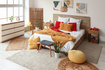 Interior of stylish bedroom with wooden tables, commode and poufs