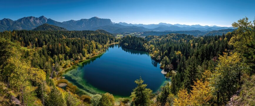 Panoramic view of a serene blue lake surrounded by autumn forests and distant mountains