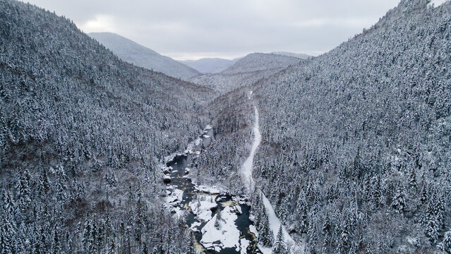 Aerial view of a snow-covered road crossing the snow-covered boreal forest and running alongside a river on a winter day. - Powered by Adobe