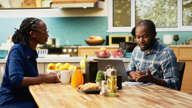 Angry boyfriend and girlfriend having argument about finances. Woman holding receipts and the man gestures in frustration, yelling and blaming each other, irresponsible money management. Camera B.