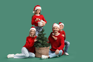 Happy family in Santa hats with Christmas tree on green background