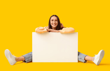 Young woman with blank poster sitting on yellow background