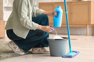 Woman with mop pouring detergent into bucket of water in room © Pixel-Shot