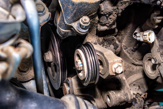 Close-up of automotive engine bay showing tensioner pulley and alternator pulley with dirt and wear