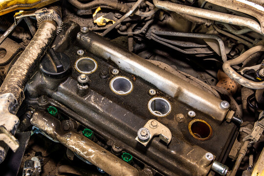 Removed valve cover of gasoline engine with spark plug holes exposed during spark plug replacement