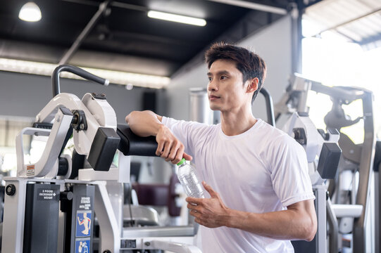 Asian man client or fitness trainer coach holding water bottle taking a rest after exercising in gym