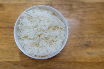 A simple white bowl filled with fluffy white steamed rice against a wood background