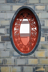 This view features an oval-shaped window set in a brick wall, showcasing intricate red decorations typical of traditional Sichuan architecture. The window adds charm and character to the building.