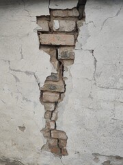 Destruction or structural damage to a wall where the plaster has peeled away, exposing the brick.