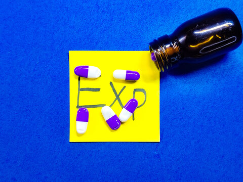 Expired medicine in pills and capsules scattered from a bottle on a blue surface