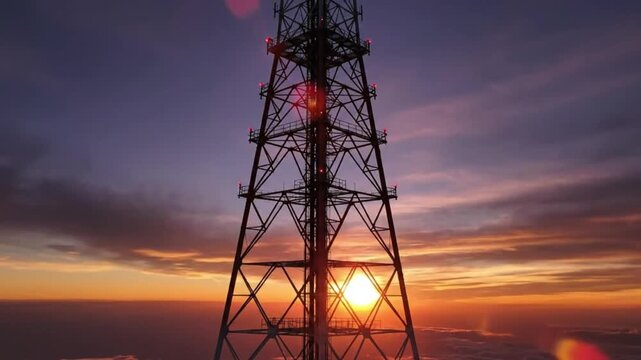 Silhouette of a tall steel lattice communication tower against a dramatic sunset sky with lens flare.