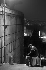Rear view of a lonely man sitting alone on a city street at night, black and white
