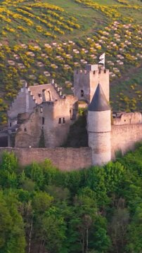 bourscheid castle ch&acirc;teau de green valley hills behind walls black domed towers flag top foggy day tall trees yellow to left near right drone panning shot 