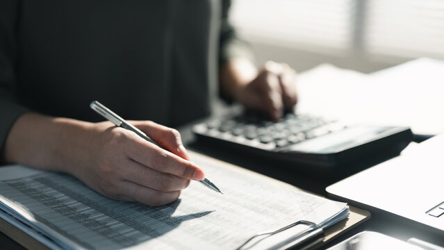Hands writing financial records and using a calculator, representing accounting tasks, budgeting plans, tax calculation, cost management, and financial reporting in a professional office setting.