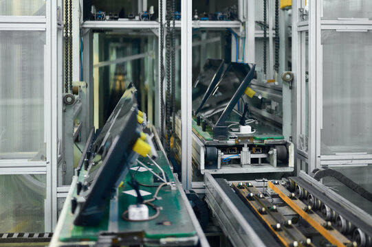 Televisions on conveyor belt in manufacturing plant with assembly machinery and production lines in operation