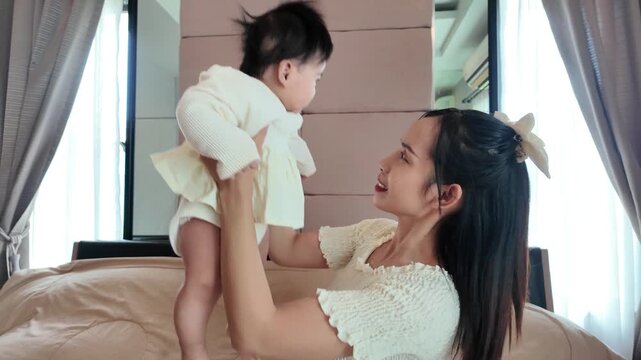 A mother happily lifting her baby up and down with both hands, creating a joyful and playful moment in a cozy environment