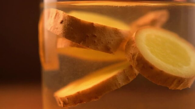 Macro shot of ginger slices floating inside a transparent glass, warm orange glow illuminating the drink