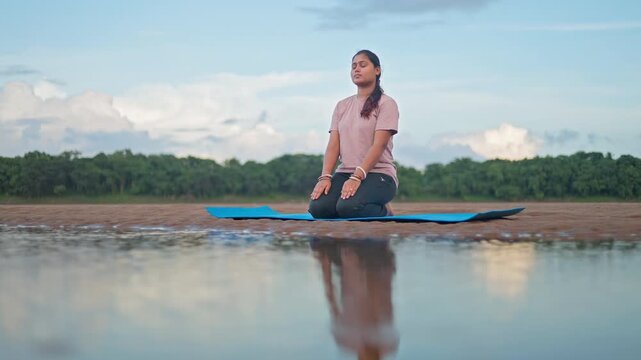 Tranquility woman performing mindful meditation in vajrasana beside a river in early morning.