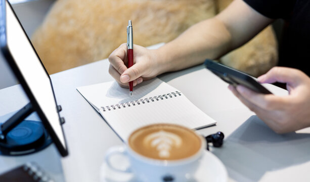 close up shot, young asian woman taking note and using mobile phone working or study online with tablet computer