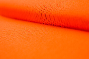 Close up of vibrant orange textile or synthetic fabric texture with small pores, folds, and deep shadow detail. Concepts of fashion material, bright color background, abstract pattern.