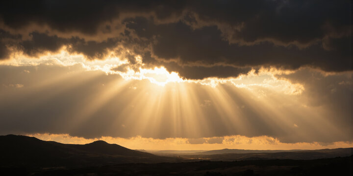 Transcendent Light Rays Awe-inspiring crepuscular rays bursting through storm clouds creating divine-like beams of golden sunlight that illuminate the landscape