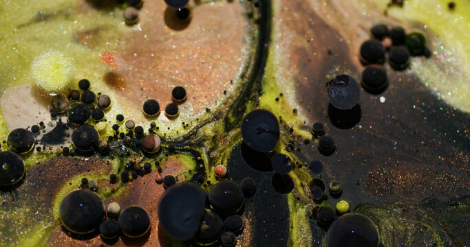 Oil bubbles. Glitter paint. Defocused yellow orange color sparkling dark black texture blend water floating on abstract bokeh art background.