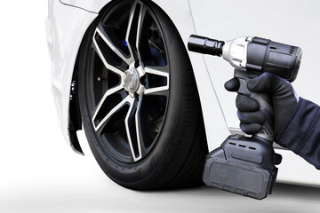Mechanic hand uses a cordless impact driver to work on a car wheel and lug nuts. Focus on tire change, auto repair, and service.