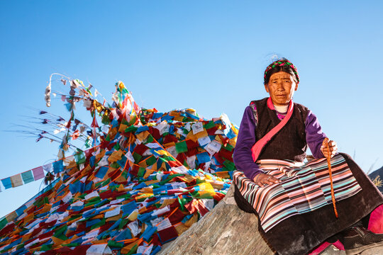 Old tibetan woman in traditional dress near prayer flags, Tibet