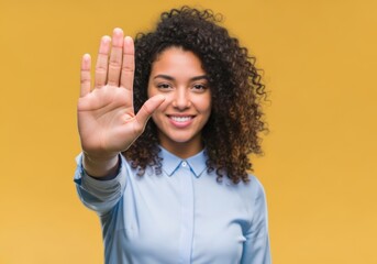A young woman with curly hair smiles confidently at the camera, holding her hand up in a stop gesture, conveying a message of assertiveness, boundaries, and refusal against a bright yellow background