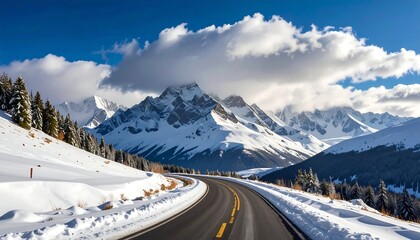 A winding asphalt road curves through a snow-covered landscape with towering, snow-capped mountains under a blue sky dotted with puffy clouds