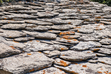 Weathered stone roof slabs featuring orange lichen within bright daylight, forming the rough layered texture